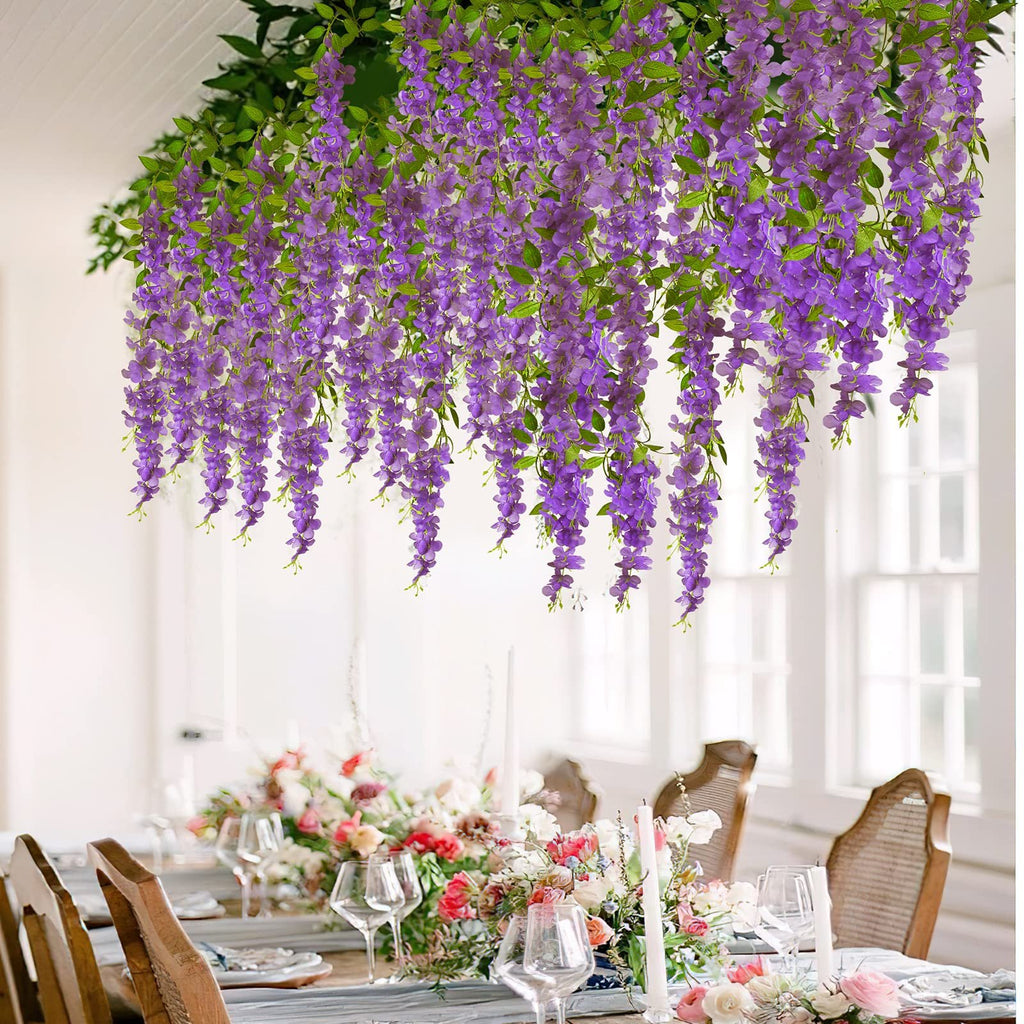 Artificial purple wisteria vines hanging over a decorated dining table with floral centerpieces and place settings.