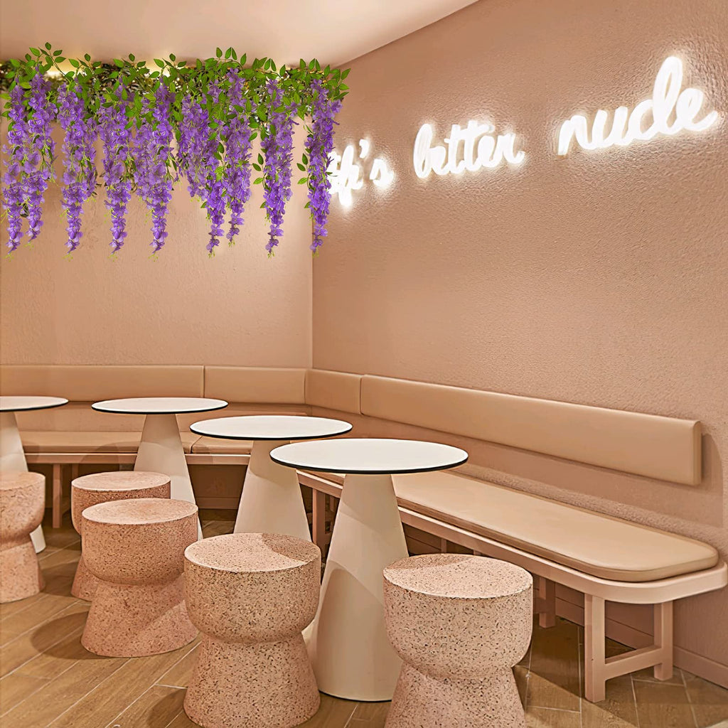 Artificial wisteria vines with purple flowers and green leaves draped across a ceiling above tables and stools in a cafe.