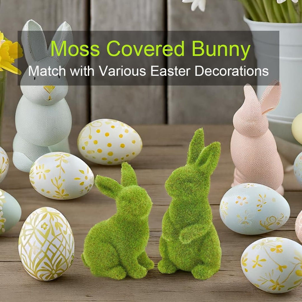 Two green moss bunnies sit among decorative Easter eggs and pastel bunnies on a wooden surface.