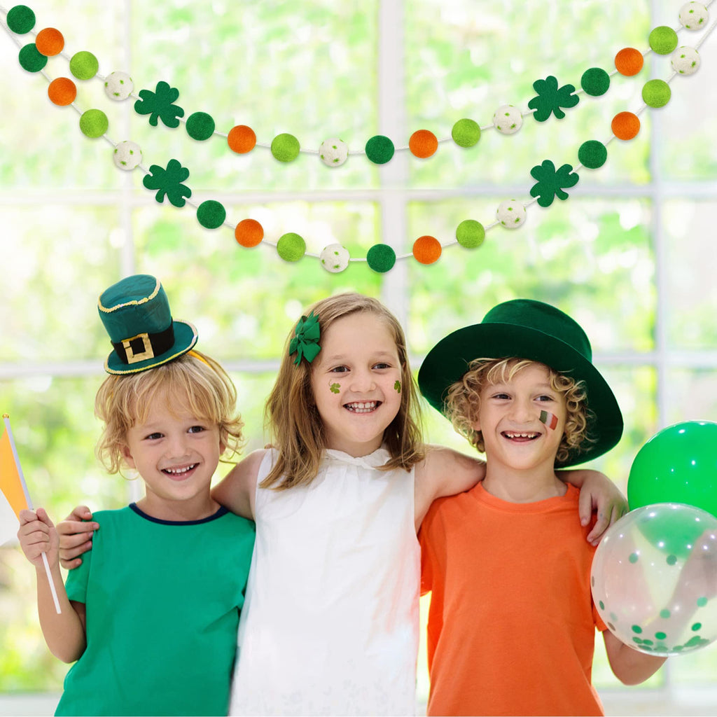Three children smiling, wearing St. Patrick's Day hats and face paint, with felt ball garlands and balloons in the background.