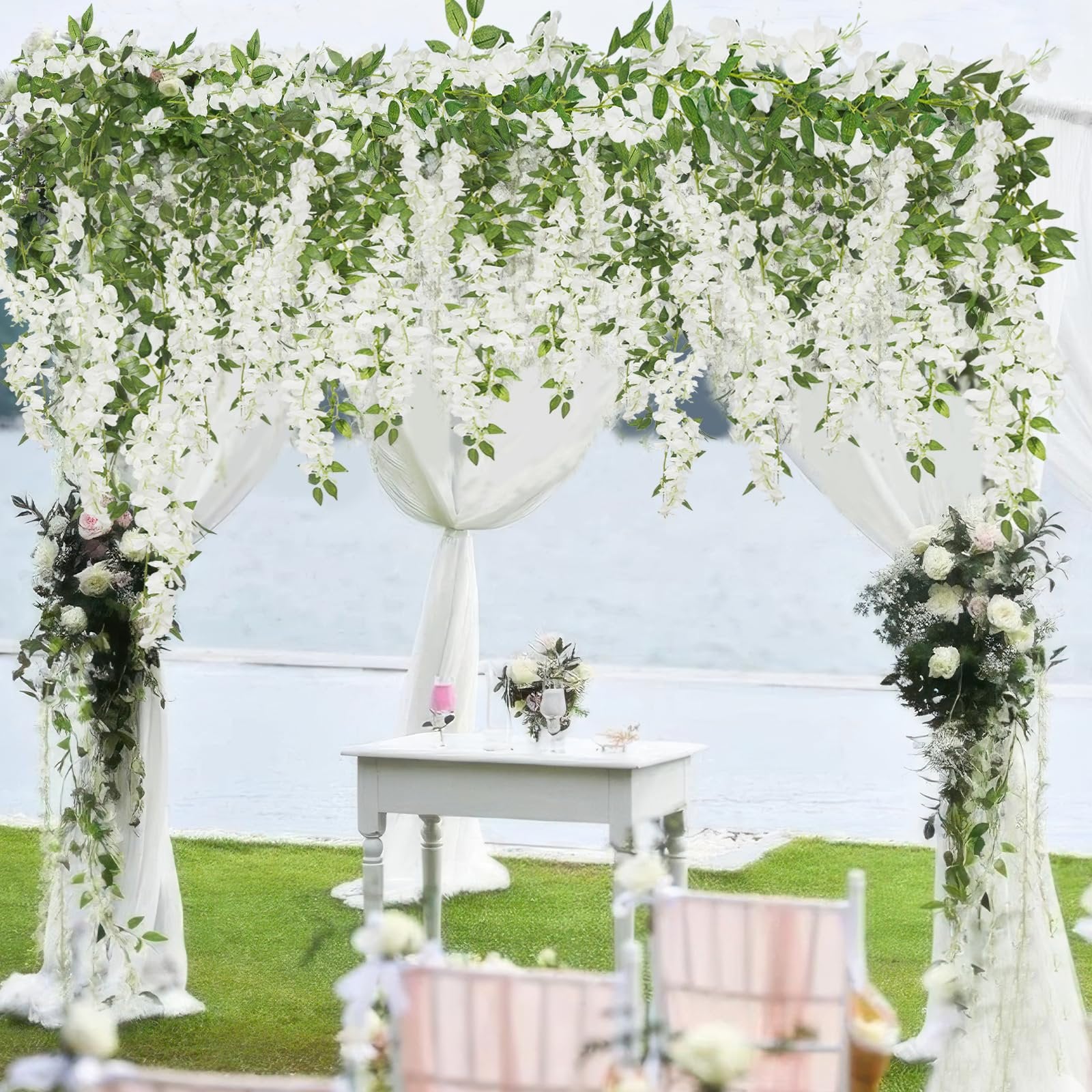 White artificial wisteria garland draped over a wedding arch with a table and chairs in the foreground.