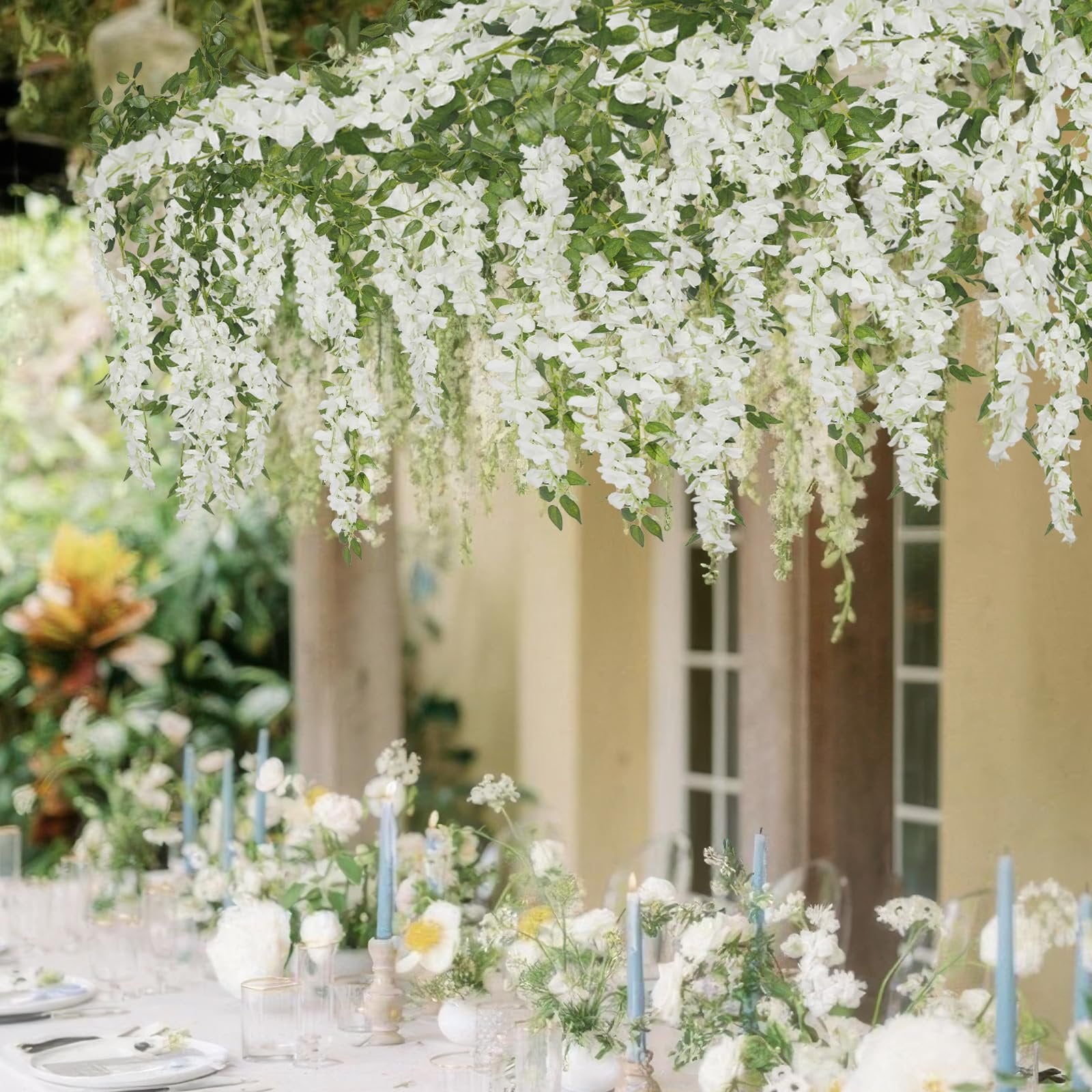 White artificial wisteria garland draped over a beautifully set table with blue candles and floral arrangements.