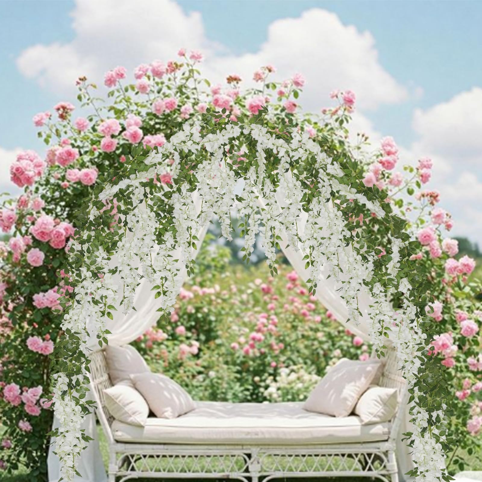 White artificial wisteria garlands draped over a wedding arch with pink roses and a white daybed