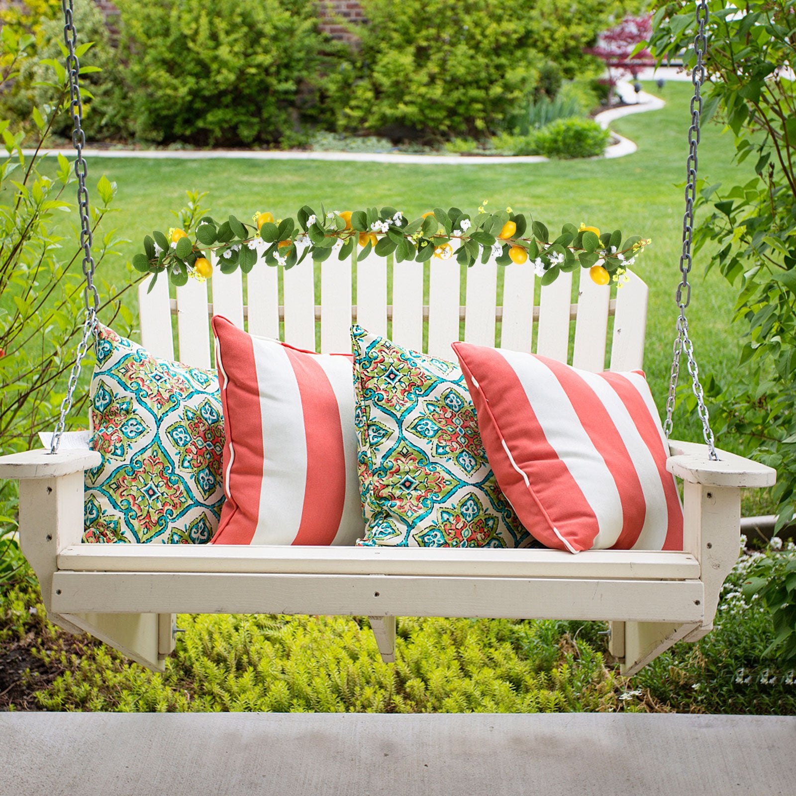 Artificial lemon vine garland with greenery and small white flowers draped over a white porch swing with decorative pillows.