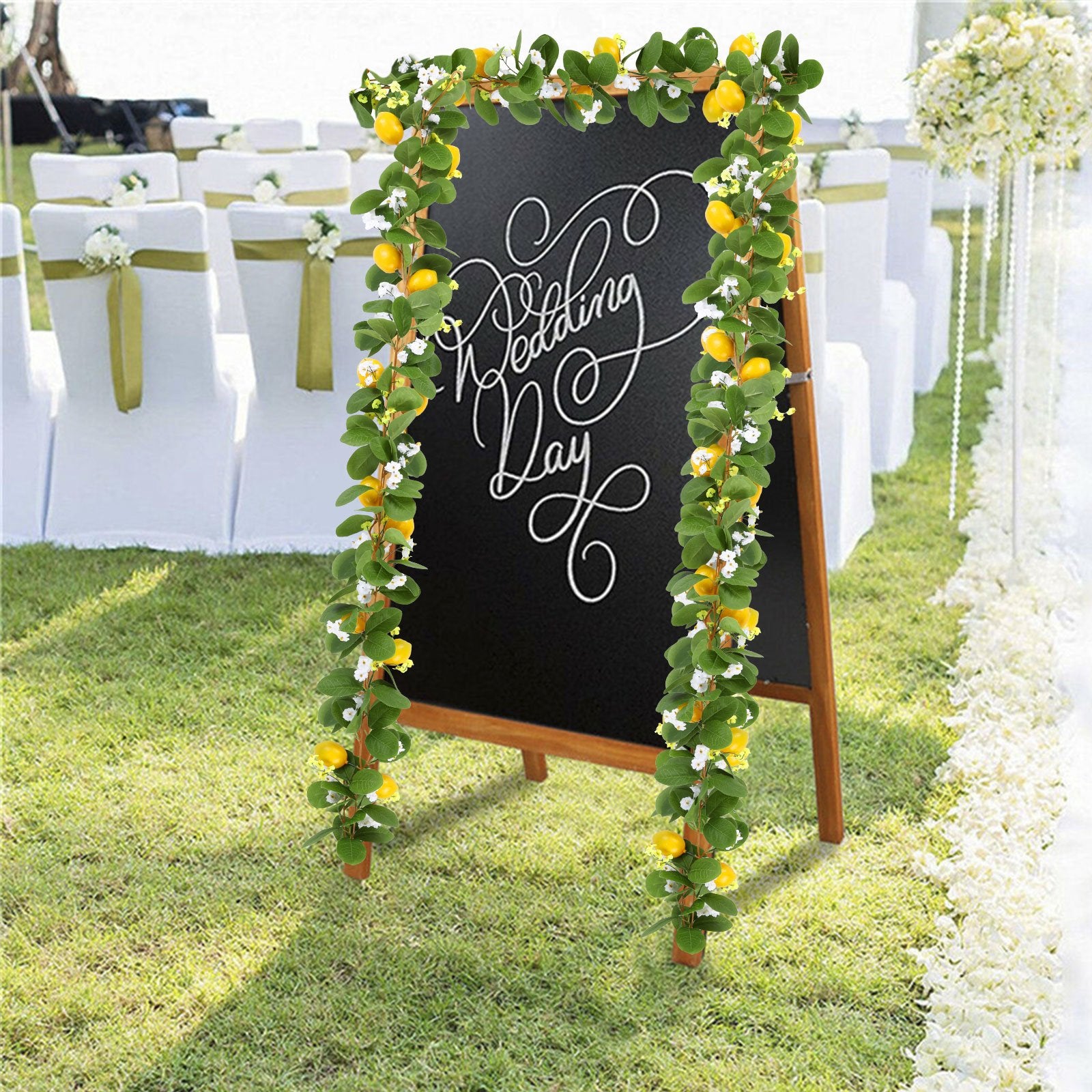 Artificial lemon vine garland with green leaves and yellow lemons draped around a chalkboard with 'Wedding Day' written on it.