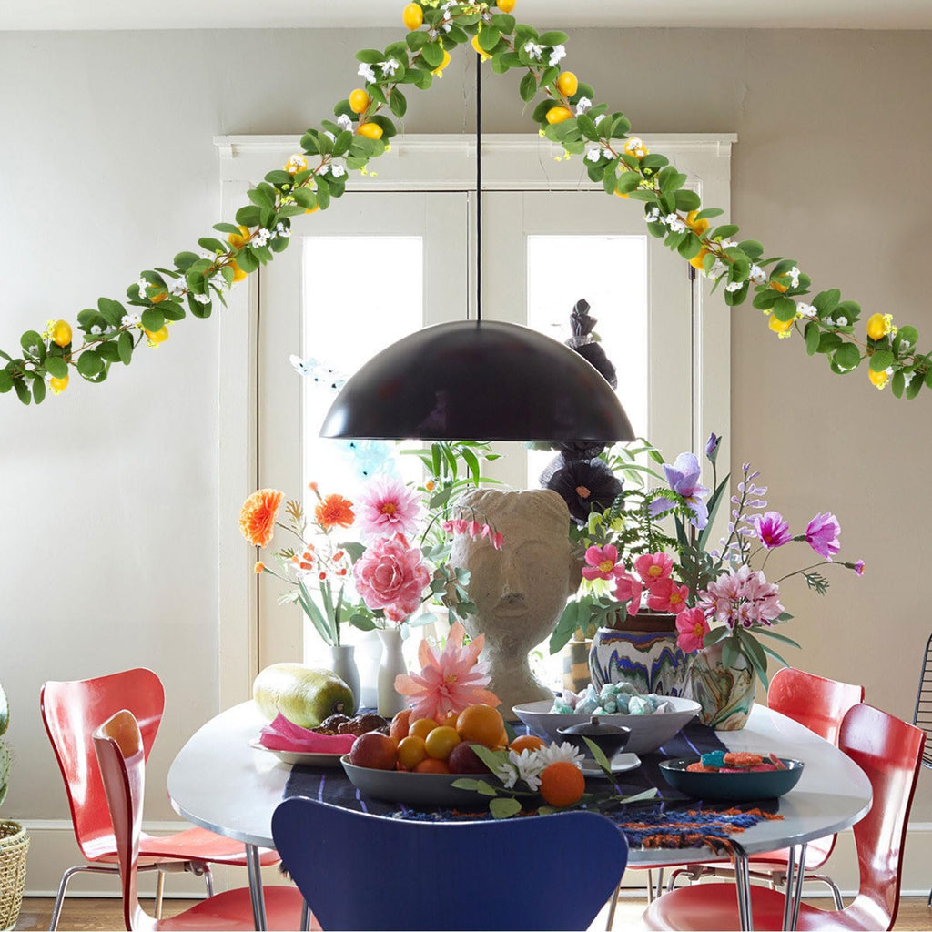 Artificial lemon vine garland draped over a dining table with flowers and fruit