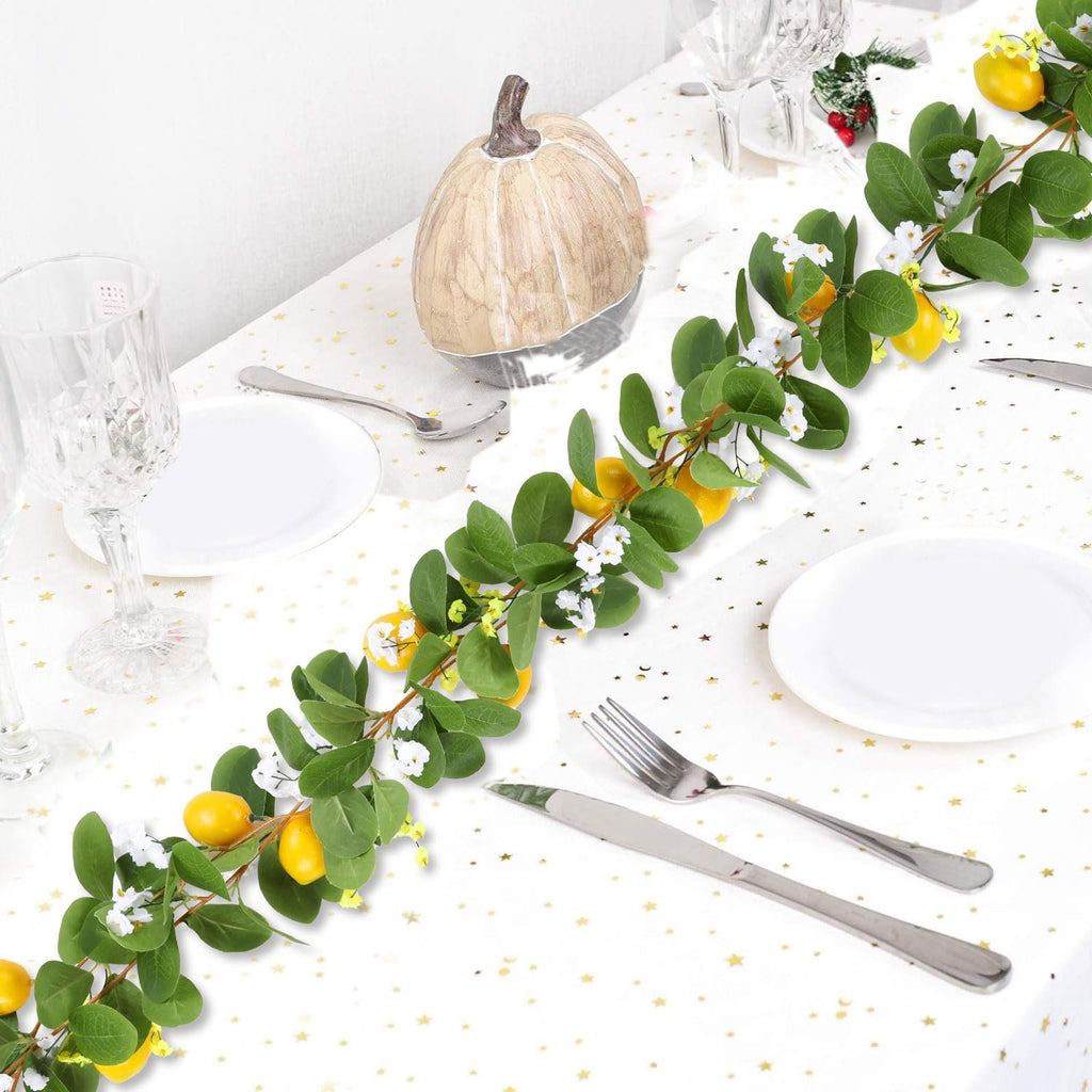 Artificial lemon vine garland with green leaves and white flowers draped across a table setting with plates and cutlery.