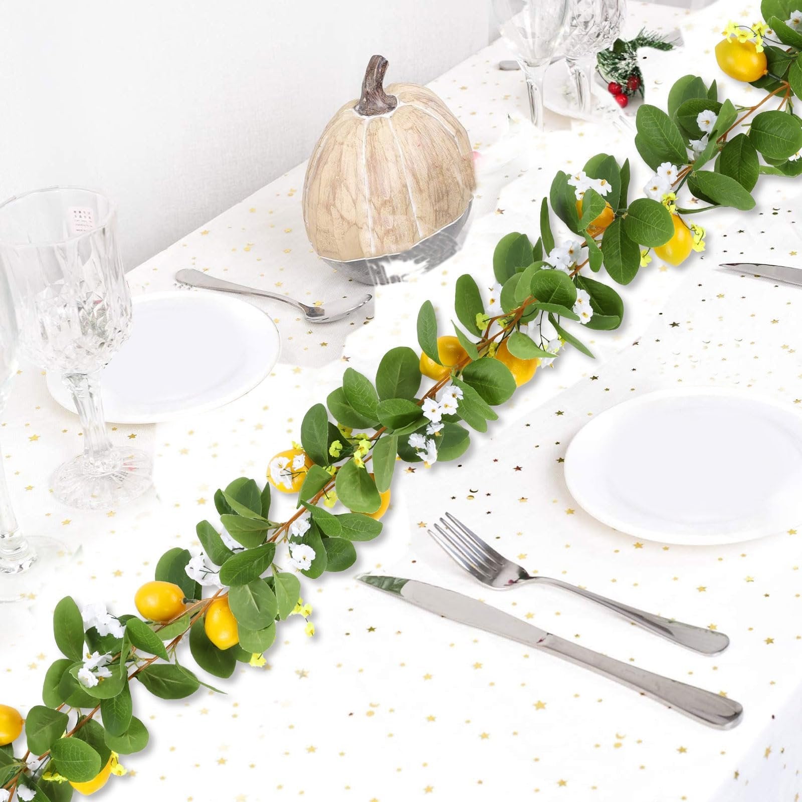 Artificial lemon vine garland with green leaves and white flowers draped across a table setting with plates and cutlery.