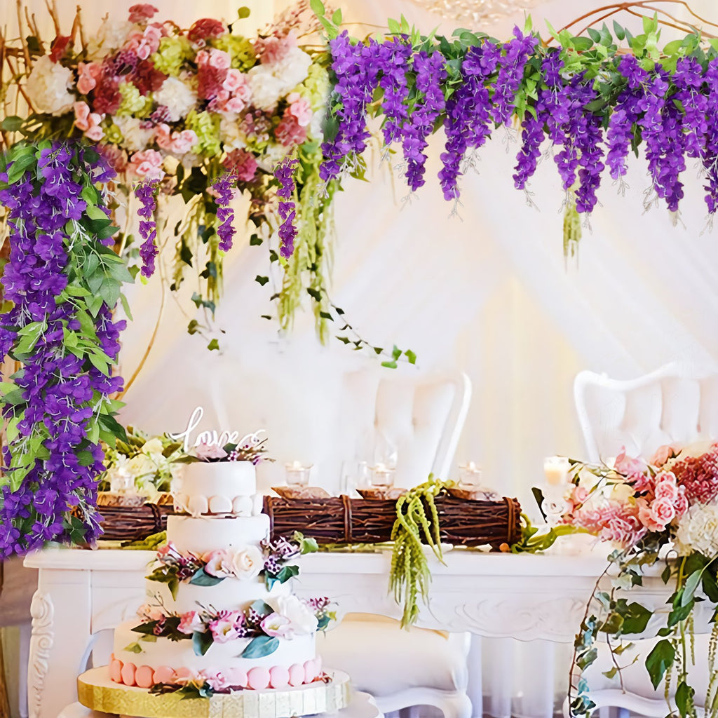 Wedding reception table decorated with purple wisteria garlands and a tiered cake with a 'love' topper.
