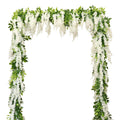 White faux wisteria garland with green leaves draped in an arch shape against a white background