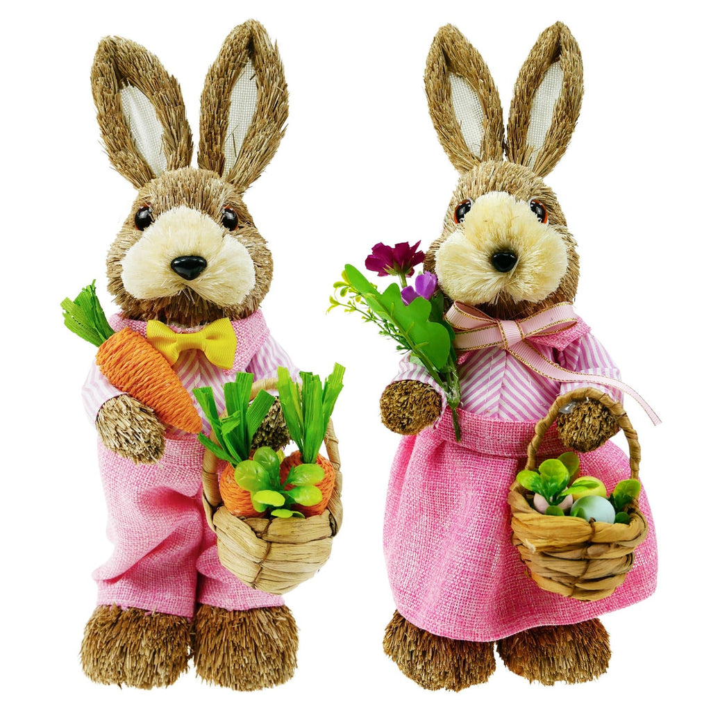 Two sisal bunny figurines in pink outfits, one holding carrots and a basket of carrots, the other holding flowers and a basket of Easter eggs.