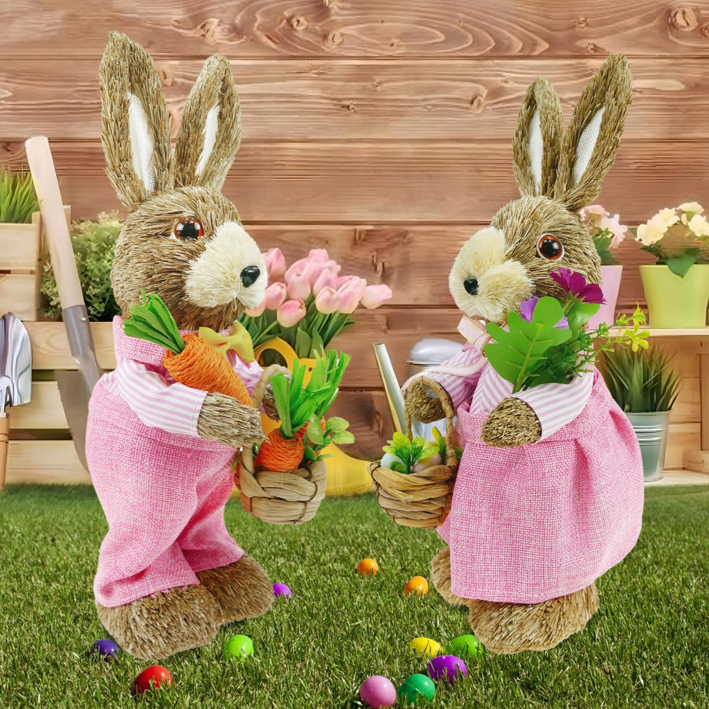 Two sisal bunny figurines in pink dresses holding Easter decorations on a grassy lawn with a wooden background.