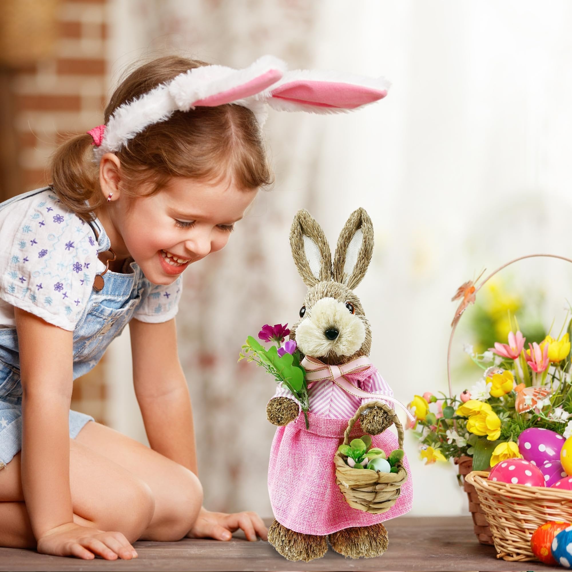 Young girl with bunny ears looking at a straw bunny figurine holding flowers and a basket with eggs, with Easter baskets and eggs in the background.