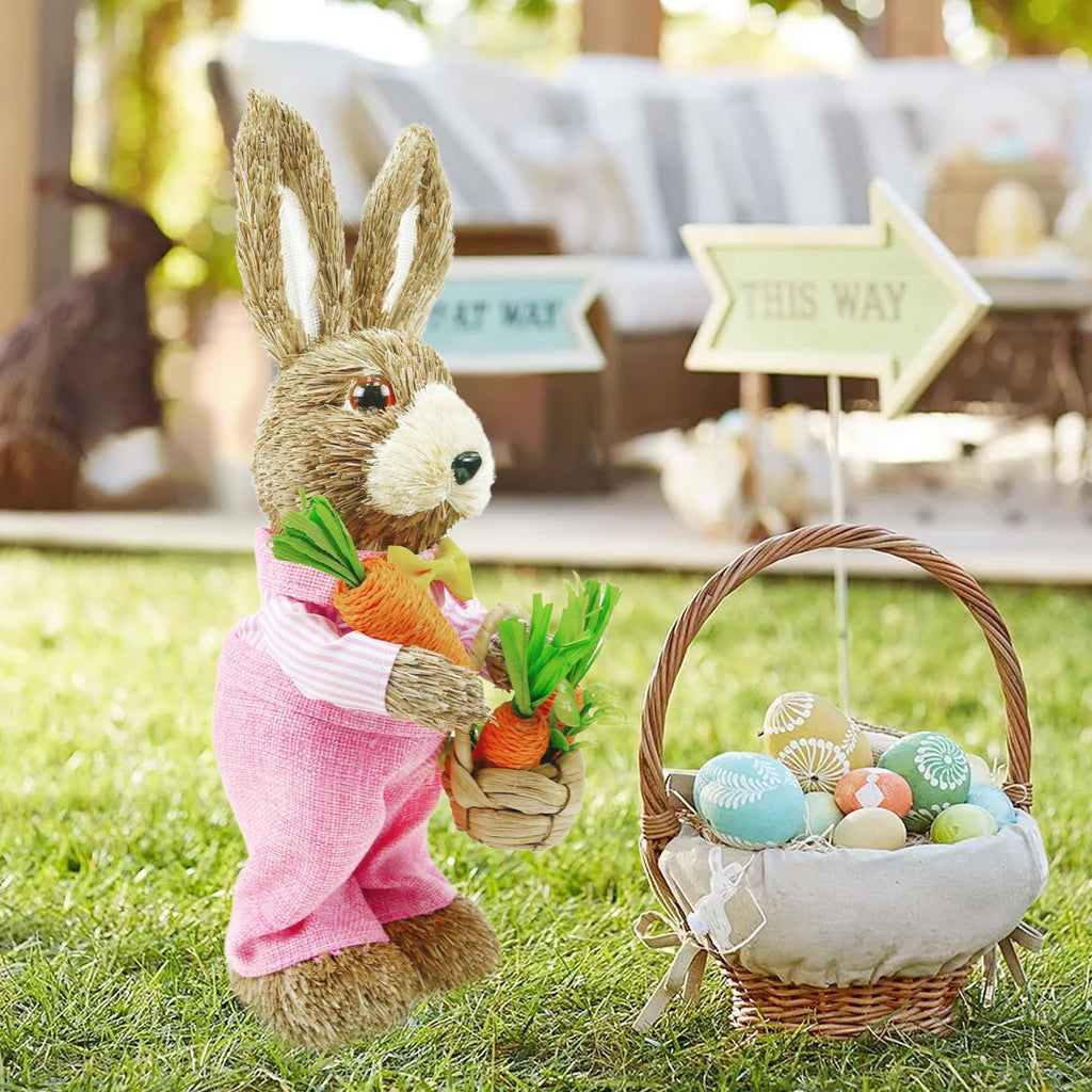 Easter bunny figurine in pink overalls holding carrots next to a basket of decorated eggs on grass