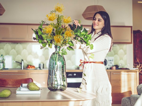 Woman arranging yellow chrysanthemum bouquet in a green vase on a table with pears and books