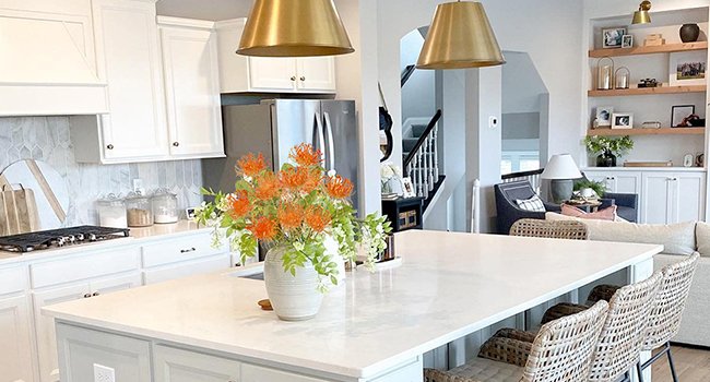 Orange artificial chrysanthemum bouquet in a vase on a kitchen island with woven bar stools