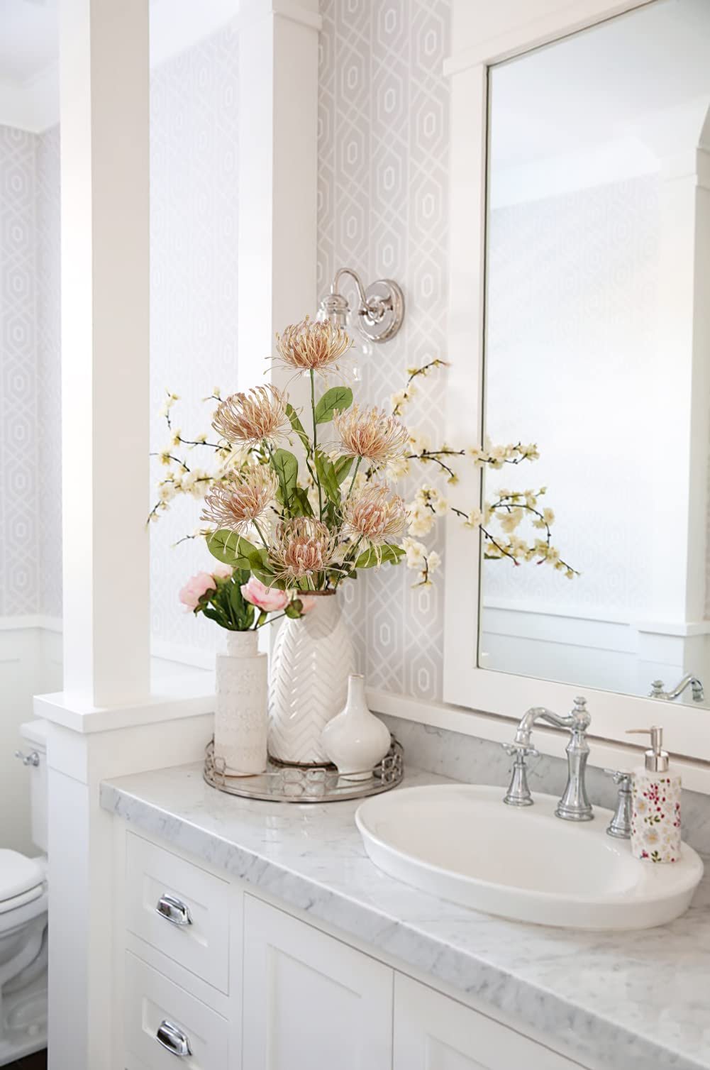 Artificial chrysanthemum bouquet in white vases on a bathroom vanity with a sink and mirror