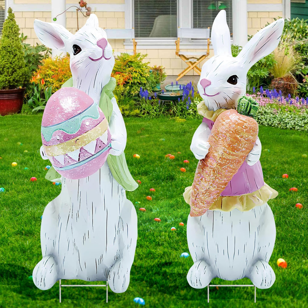 Two white Easter bunny yard signs with metal stakes in a grassy yard with Easter eggs scattered around.