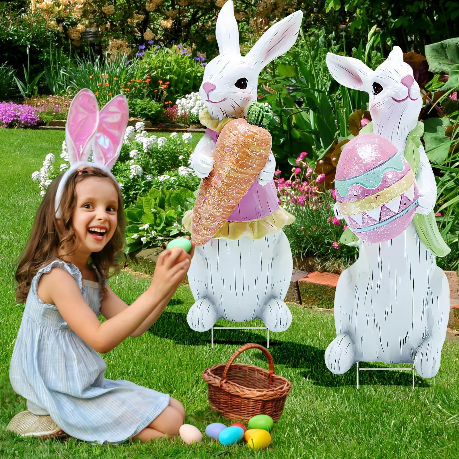 Girl with bunny ears holding an Easter egg near two large bunny yard decorations in a garden