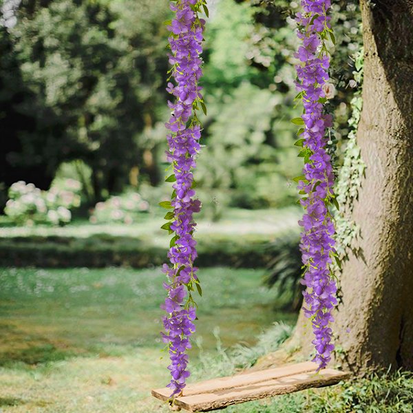 Two strands of artificial purple wisteria flowers hang beside a tree trunk with a wooden swing below.
