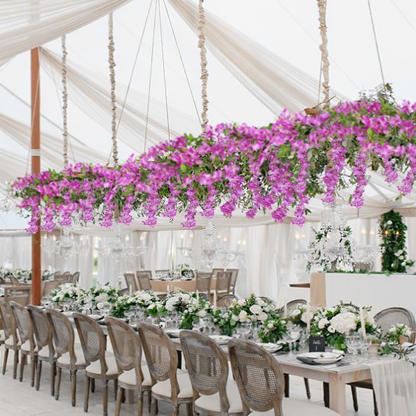 Artificial wisteria flower vines draped over a long table setting with chairs and floral arrangements.