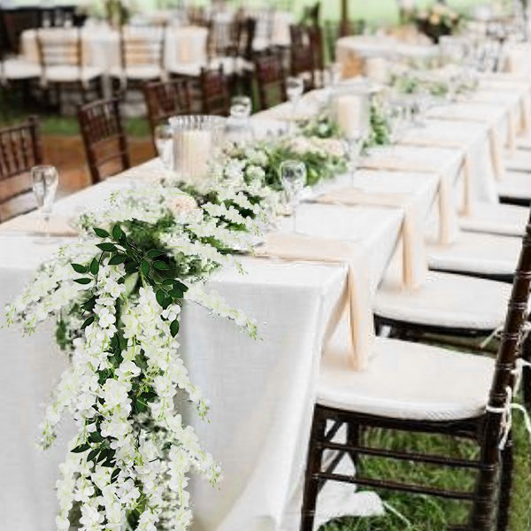 White artificial wisteria flower vines draped across a long table set for a wedding reception.