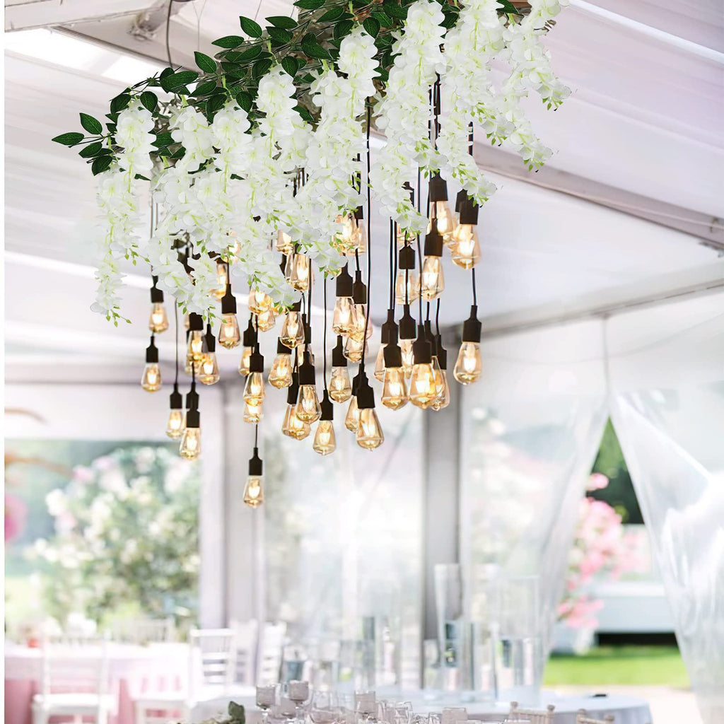 White artificial wisteria flower vines with Edison bulbs hanging above a decorated table setting