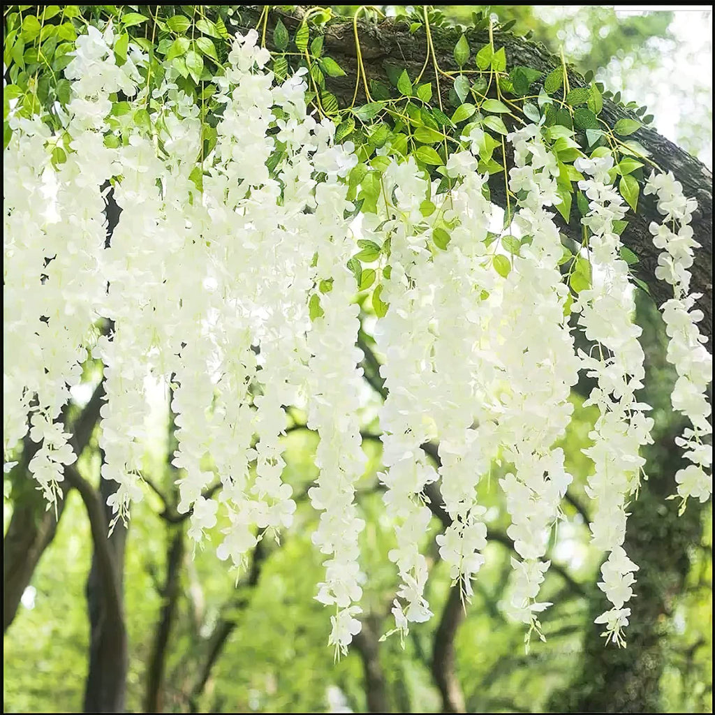 White artificial wisteria flower vines with green leaves hanging from a tree branch outdoors