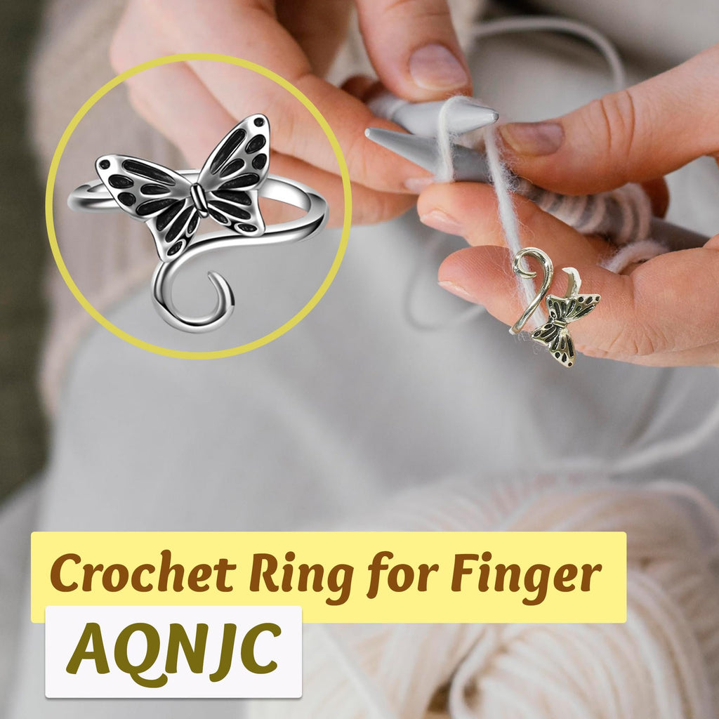 Close-up of a butterfly-shaped yarn tension ring on a finger, with knitting needles and yarn in the background.