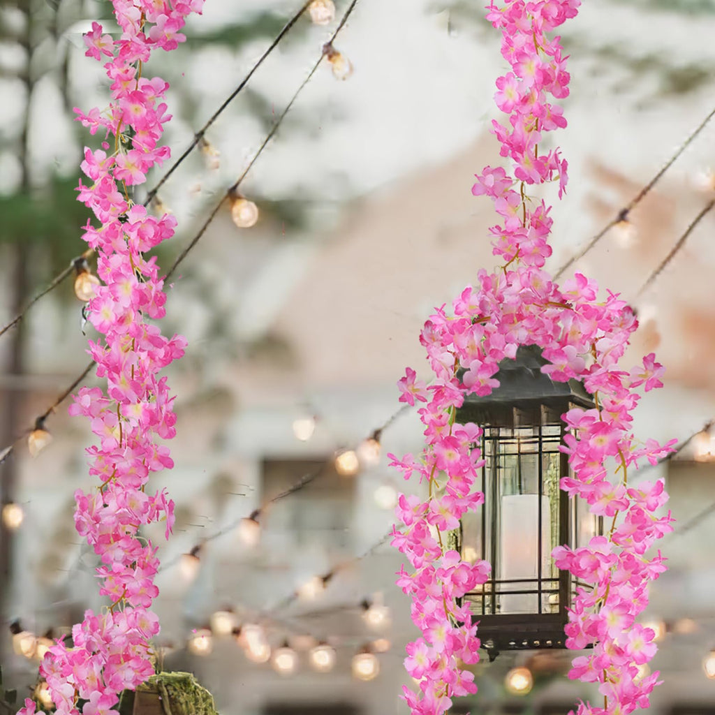 Two strands of artificial pink cherry blossom garland draped around a lantern with string lights in the background.
