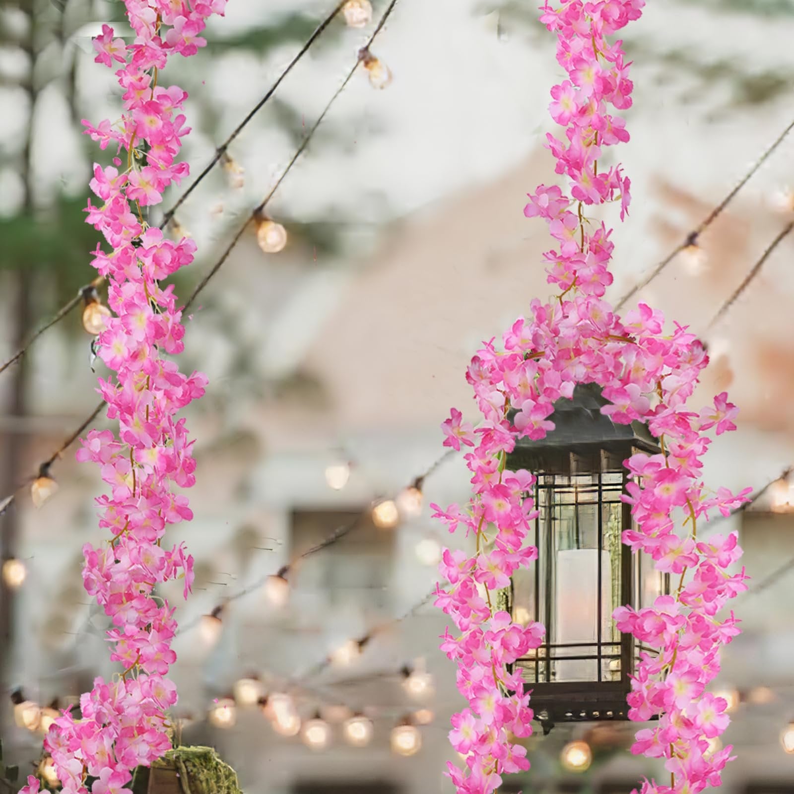 Two strands of artificial pink cherry blossom garland draped around a lantern with string lights in the background.