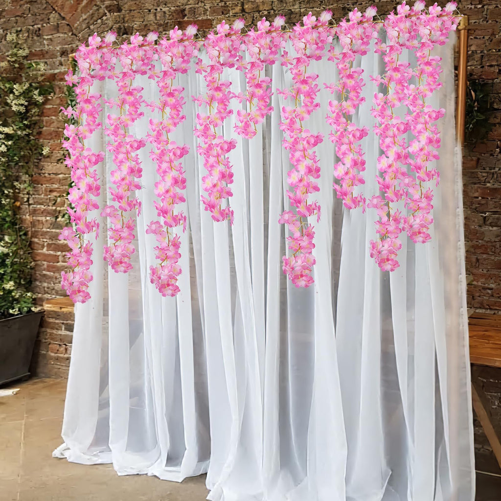 Pink cherry blossom garlands hanging against white sheer curtains and a brick wall backdrop