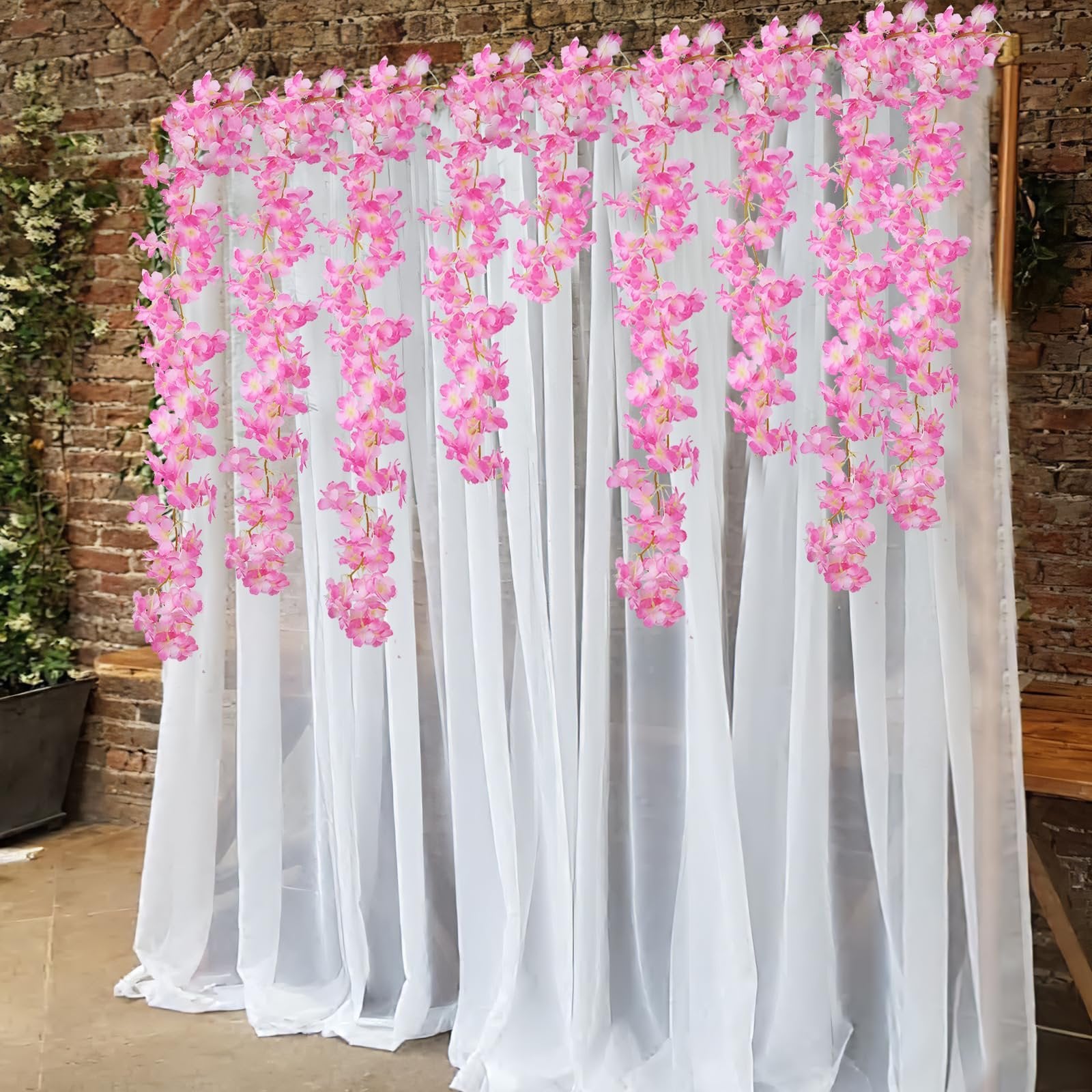 Pink cherry blossom garlands hanging against white sheer curtains and a brick wall backdrop