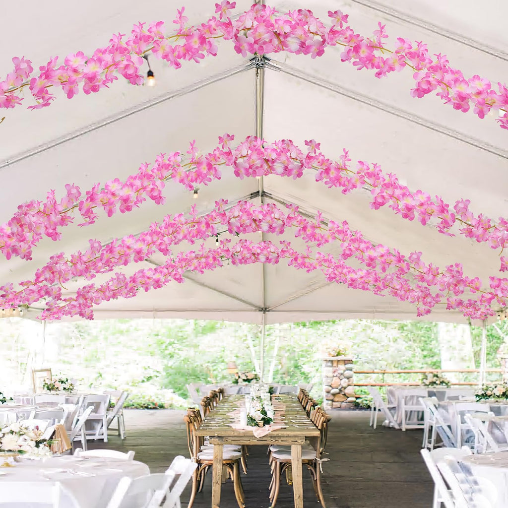 Pink cherry blossom garlands draped inside a tent over tables set for an event