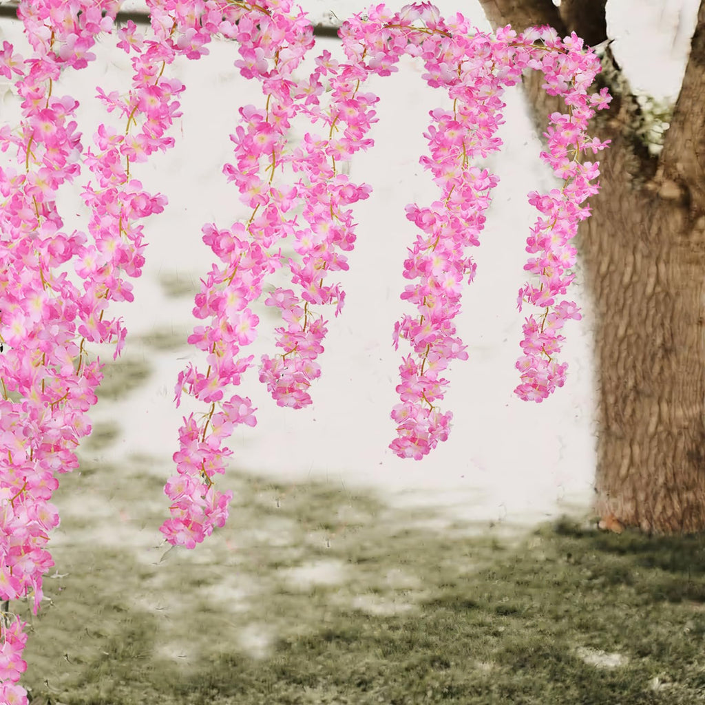 Two strands of artificial pink cherry blossom garland hanging in front of a tree trunk and grassy area.