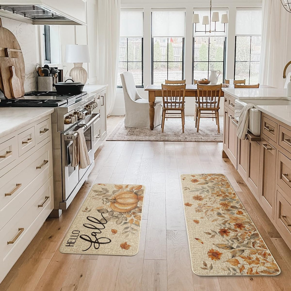 Two fall-themed kitchen mats with pumpkins and leaves on a wooden floor in a kitchen.