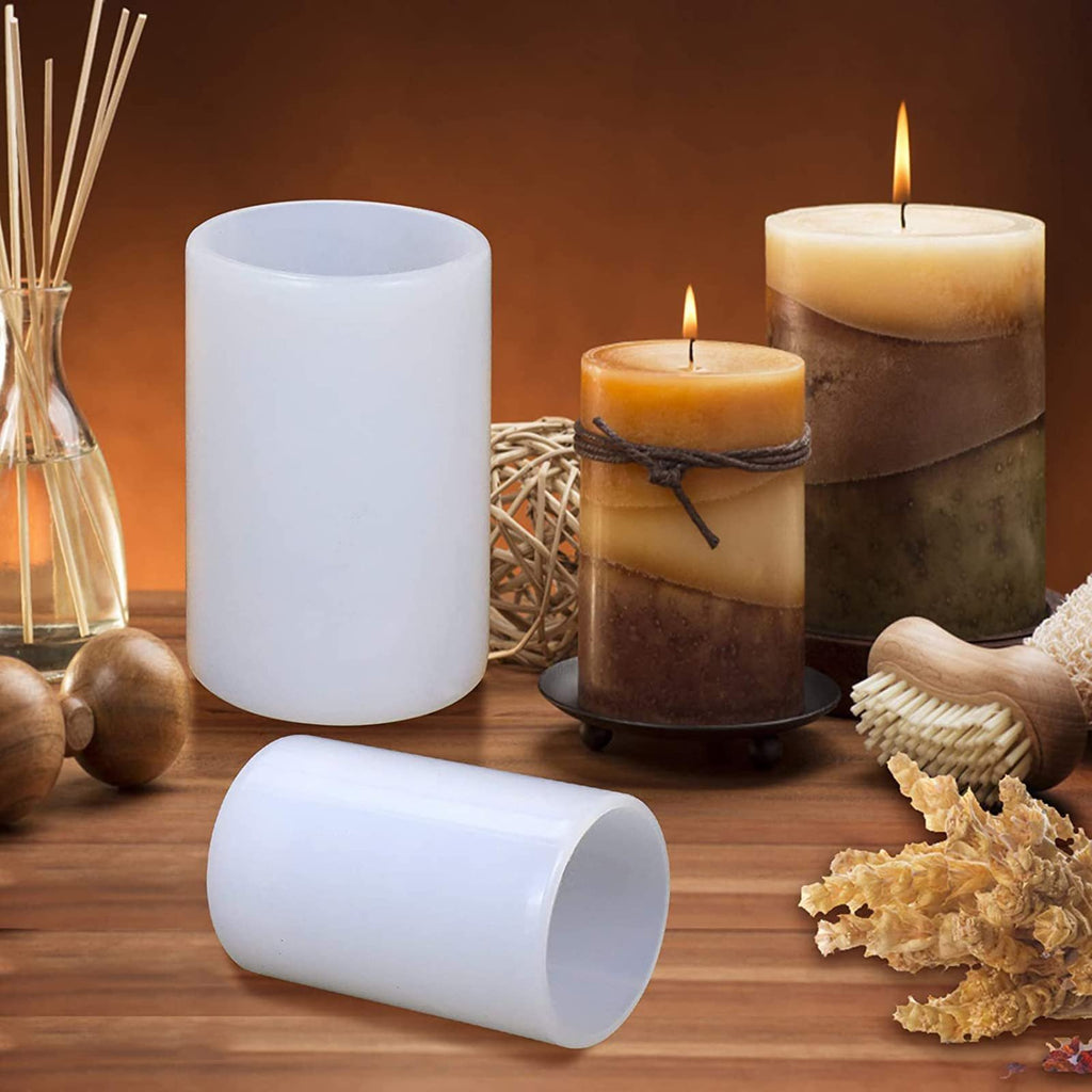 Two white silicone cylinder molds on a wooden surface with decorative elements and lit candles