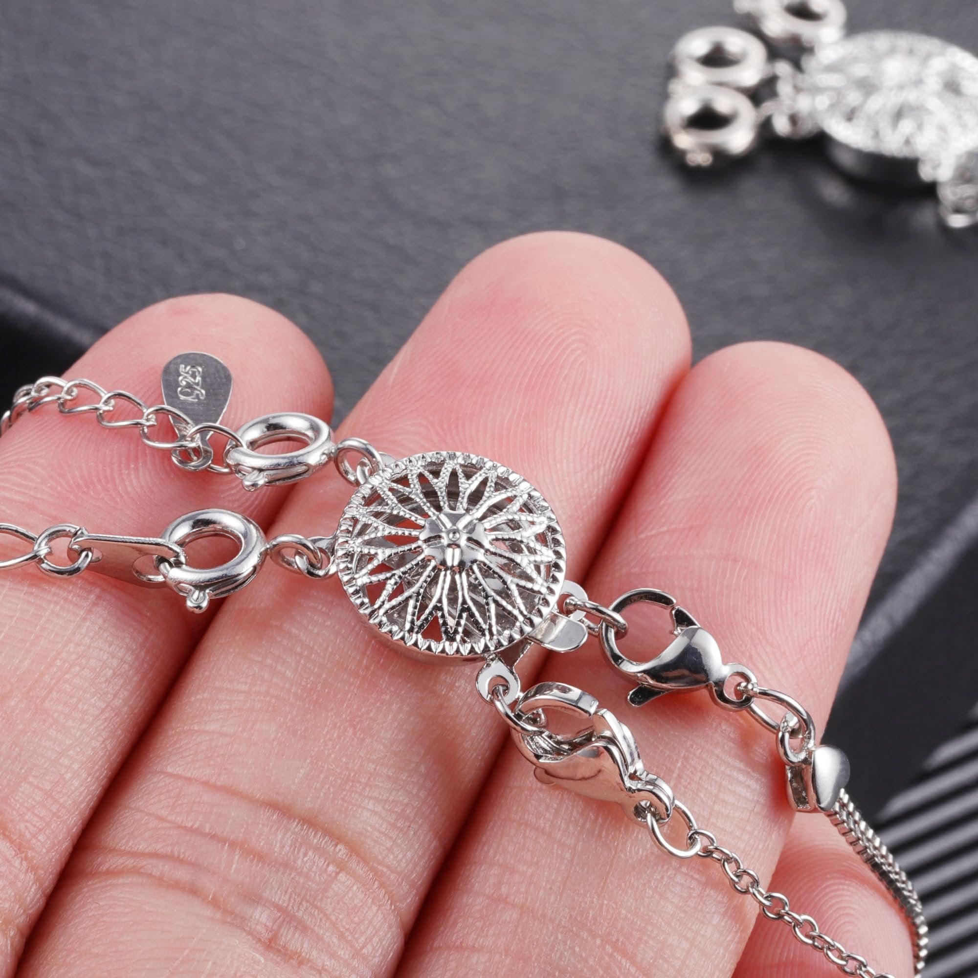 Close-up of a white gold plated brass necklace layering clasp set held by fingers, showing intricate detail and clasps.