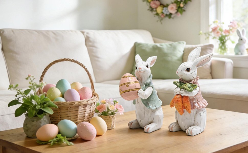 Two hand-painted resin Easter bunny figurines on a wooden table with a basket of pastel eggs and greenery.