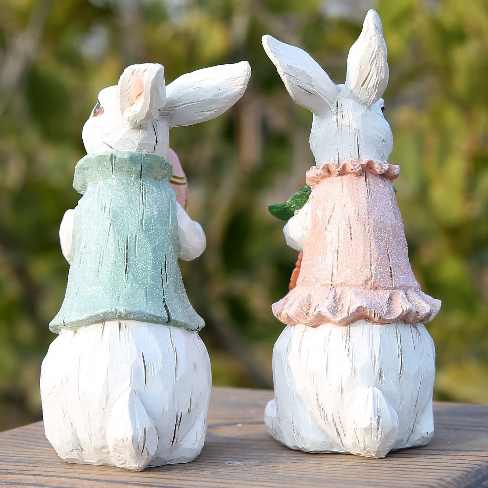 Two hand-painted resin Easter bunny figurines, one in a green vest holding a pink egg, the other in a pink dress holding a carrot.