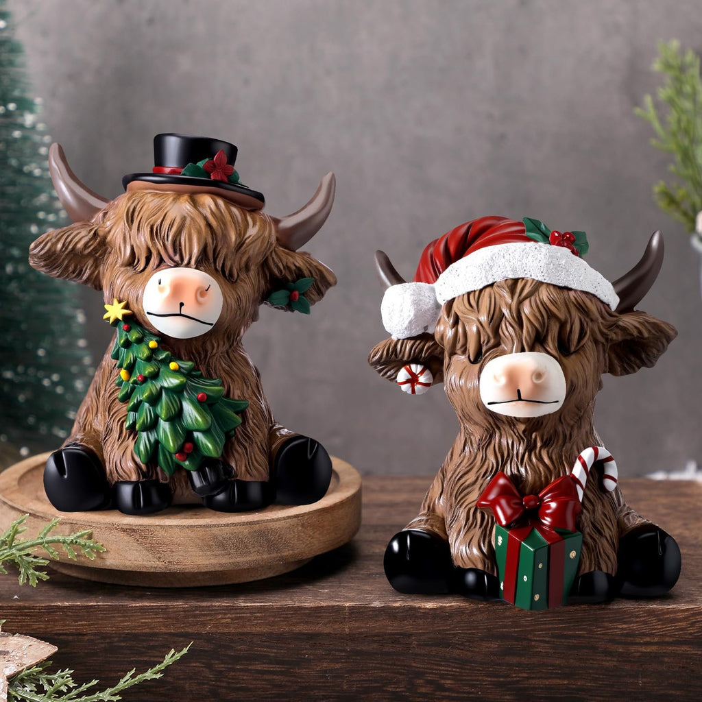 Two resin highland cow figurines dressed for Christmas, one with a top hat and tree, the other with a Santa hat and gift.