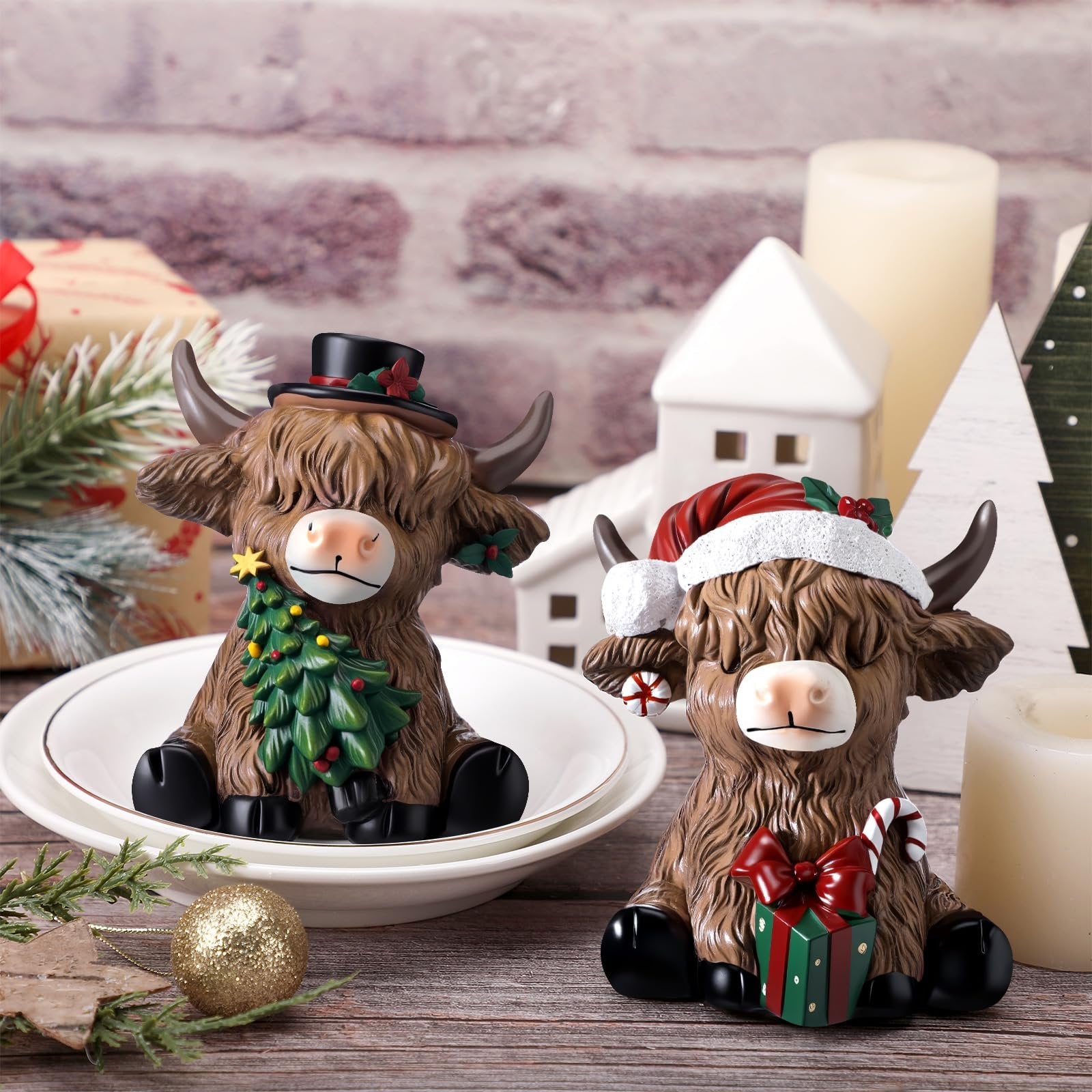 Two resin highland cow figurines dressed for Christmas, one with a top hat and tree, the other with a Santa hat and gift.