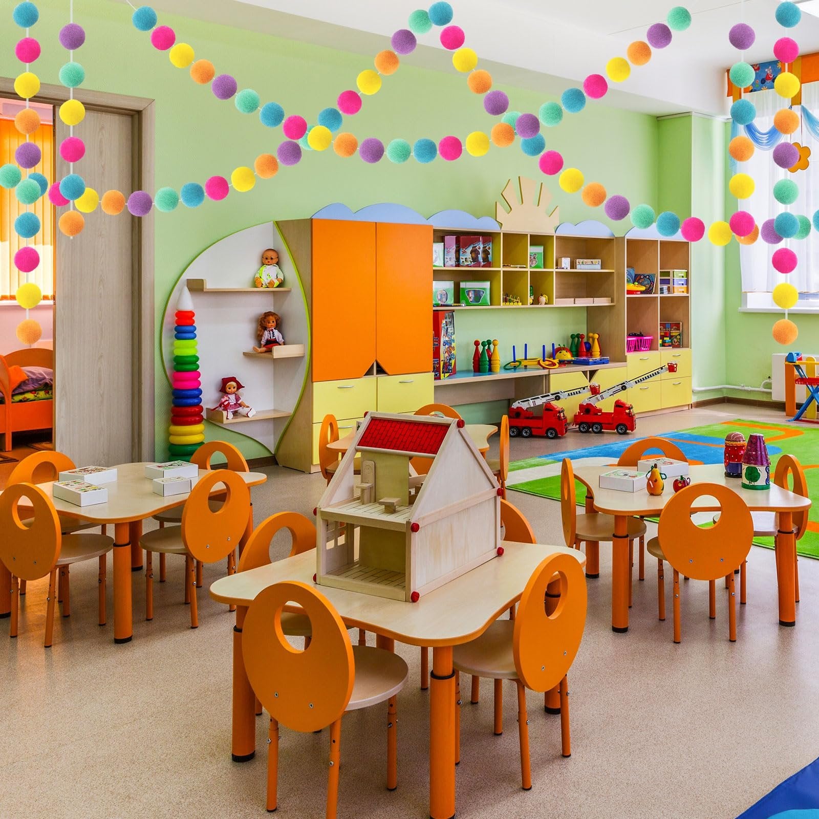 Colorful wool felt ball garlands strung across a classroom ceiling above tables and chairs.