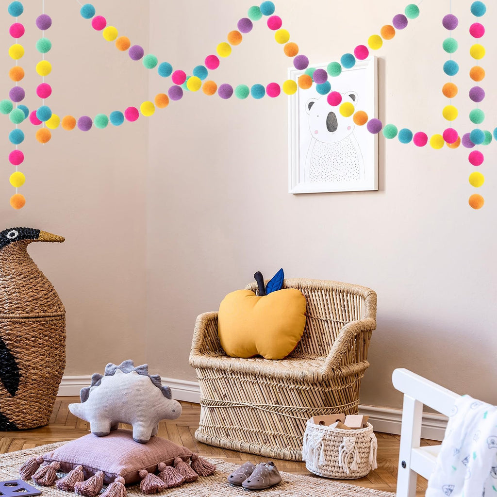 Colorful wool felt ball garlands draped across a wall above a child's chair and decor.