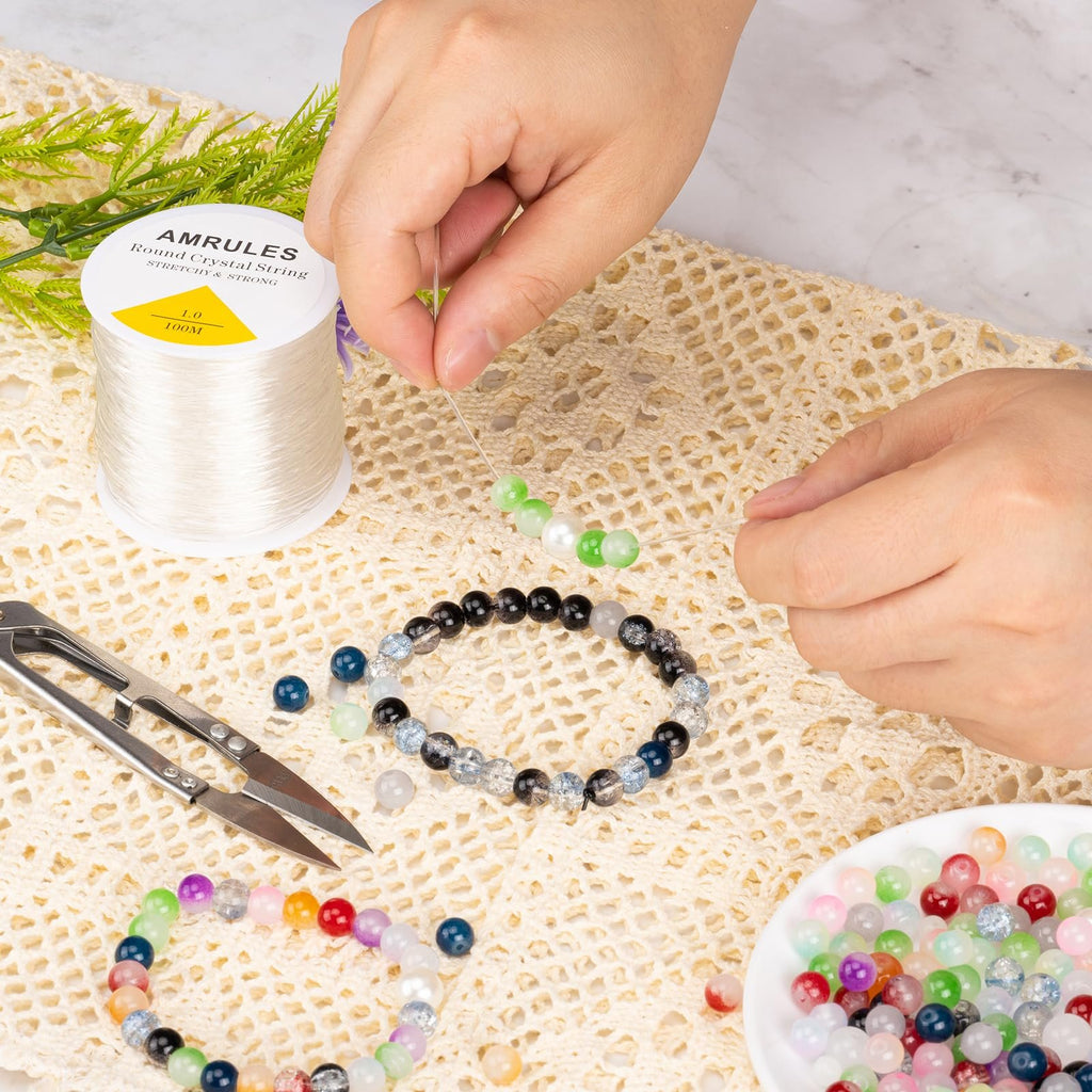 Hands stringing beads onto elastic cord with a spool of white cord and finished bracelets nearby.