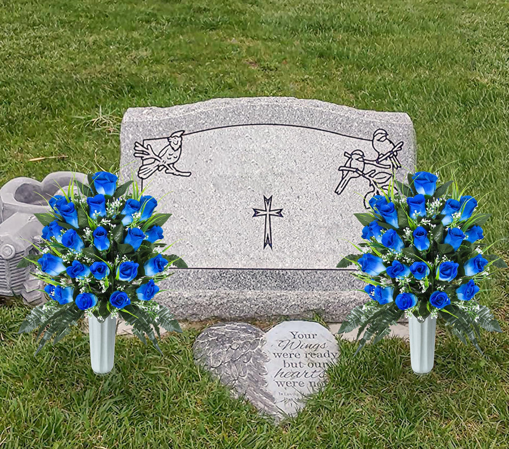 Two bouquets of blue artificial roses in vases placed in front of a granite headstone with carved birds and a cross.