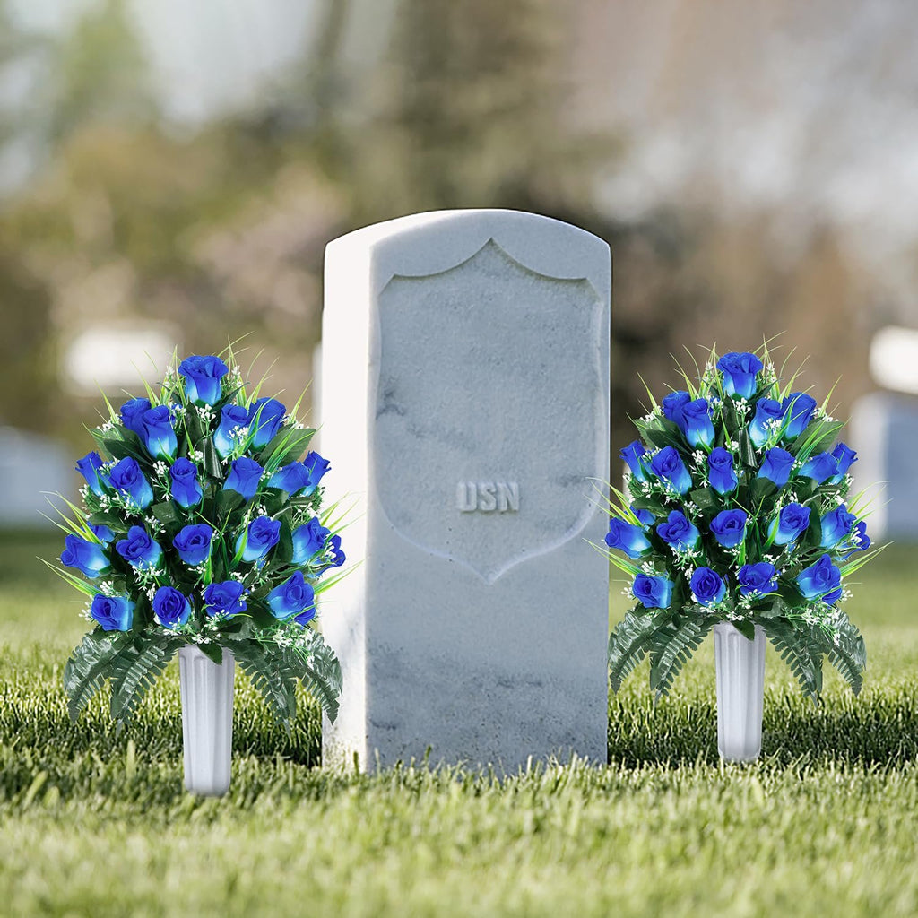 Two bouquets of blue artificial roses in white vases placed on grass in front of a tombstone with 'USN' inscription.