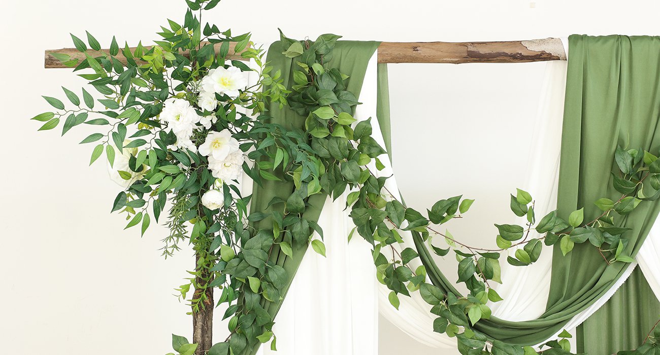 Artificial greenery garland with white flowers draped over wooden beams and fabric.
