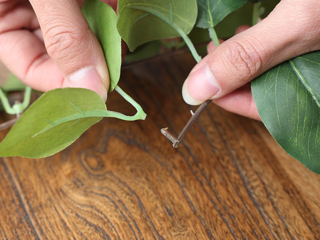 Hands arranging artificial green vine garland with silk leaves on a wooden surface