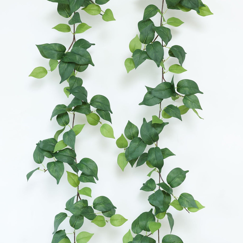 Two strands of artificial green vines with silk leaves against a white background.